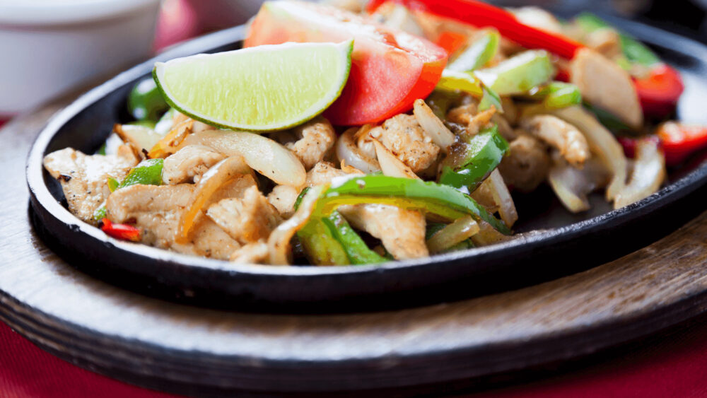 A close up image of fajitas in a cast iron pan with sources of vitamin C.
