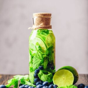 An up close image of a bottle filled with sparkling water, blueberries, ginger and lime slices.