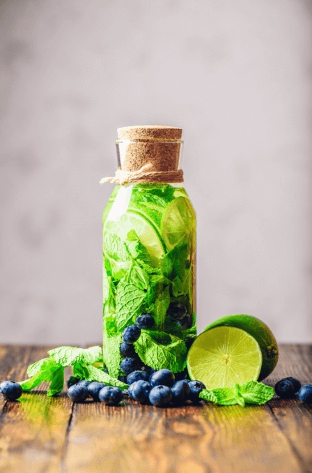 An up close image of a bottle filled with sparkling water, blueberries, ginger and lime slices.