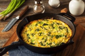 A close up image of a frittata made with asparagus and mushrooms in the cast iron skillet the dish was cooked in.