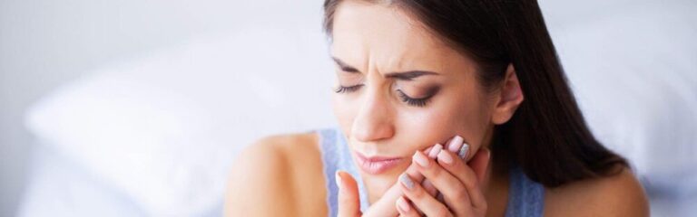 A close up image of a woman cradling her mouth in pain