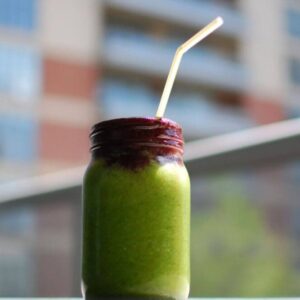 A close up image of a green smoothie with a straw that is in front of a blurred city landscape