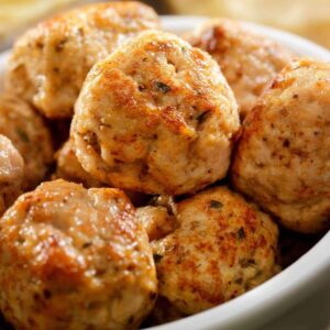 A close-up of golden-brown turkey meatballs seasoned with herbs, arranged in a white bowl.