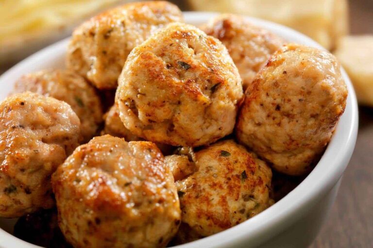 A close-up of golden-brown turkey meatballs seasoned with herbs, arranged in a white bowl.