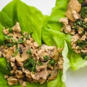 Two vibrant green lettuce leaves serve as wraps, filled with a savory mixture of ground turkey, chopped mushrooms, and fresh herbs. The filling is evenly distributed and garnished with finely chopped parsley, providing a fresh and appetizing presentation. The dish is arranged on a white plate, highlighting the colorful and healthy ingredients, making it an appealing option for those with IBD.