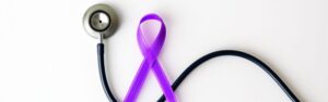 Close-up of a stethoscope and purple awareness ribbon on a white background representing inflammatory bowel disease awareness and diagnosis